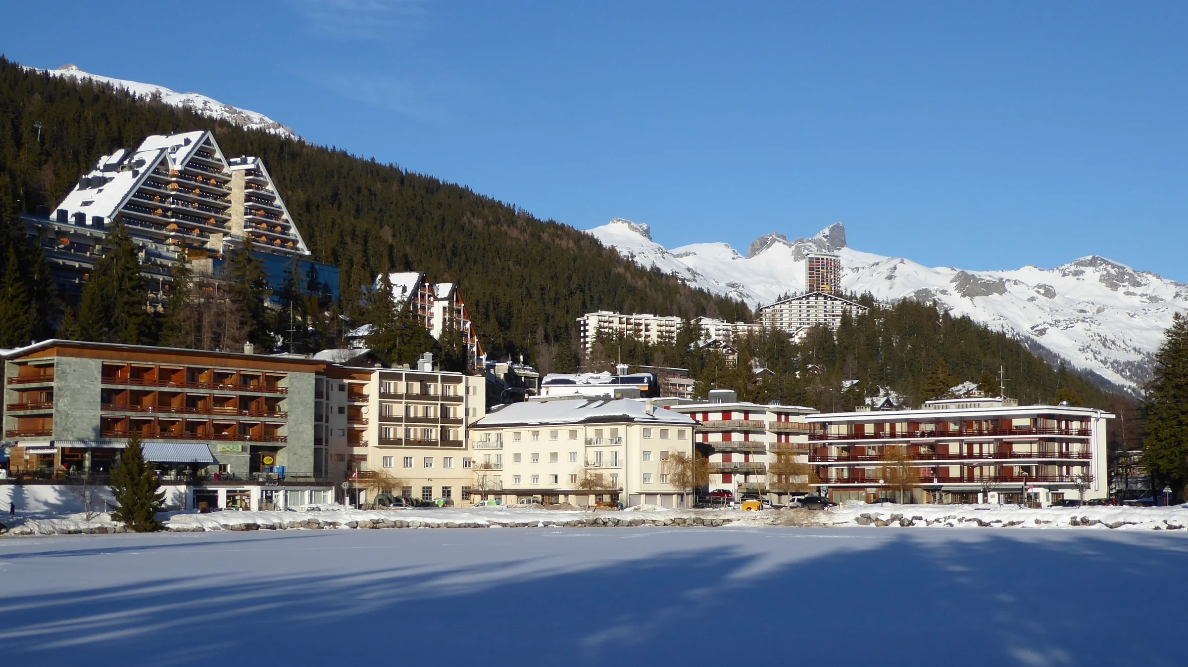 Hotels von Crans-Montana an einem zugefrorenen, verschneiten Teich unter blauem Januarhimmel.