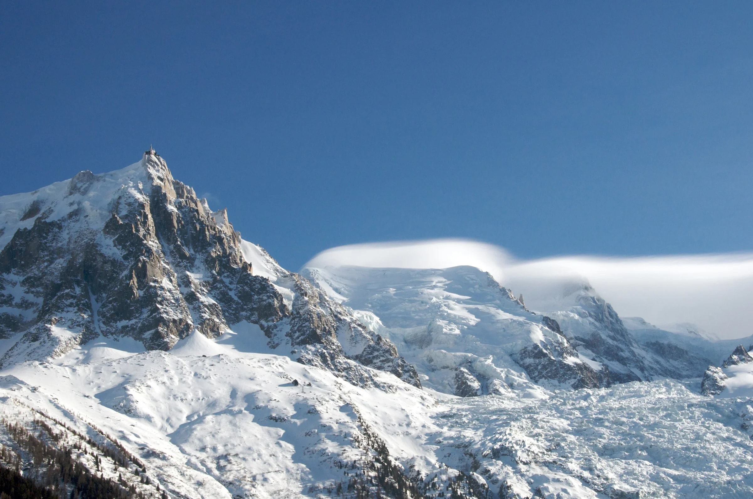 Die Aiguille du Midi und der verschneite Bossons-Gletscher über Chamonix unter blauem Himmel.