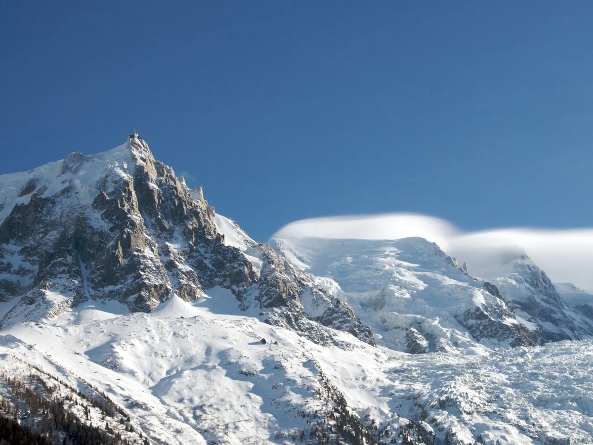 The Aiguille du Midi and the snow-covered Bossons glacier above Chamonix, under a blue sky.
