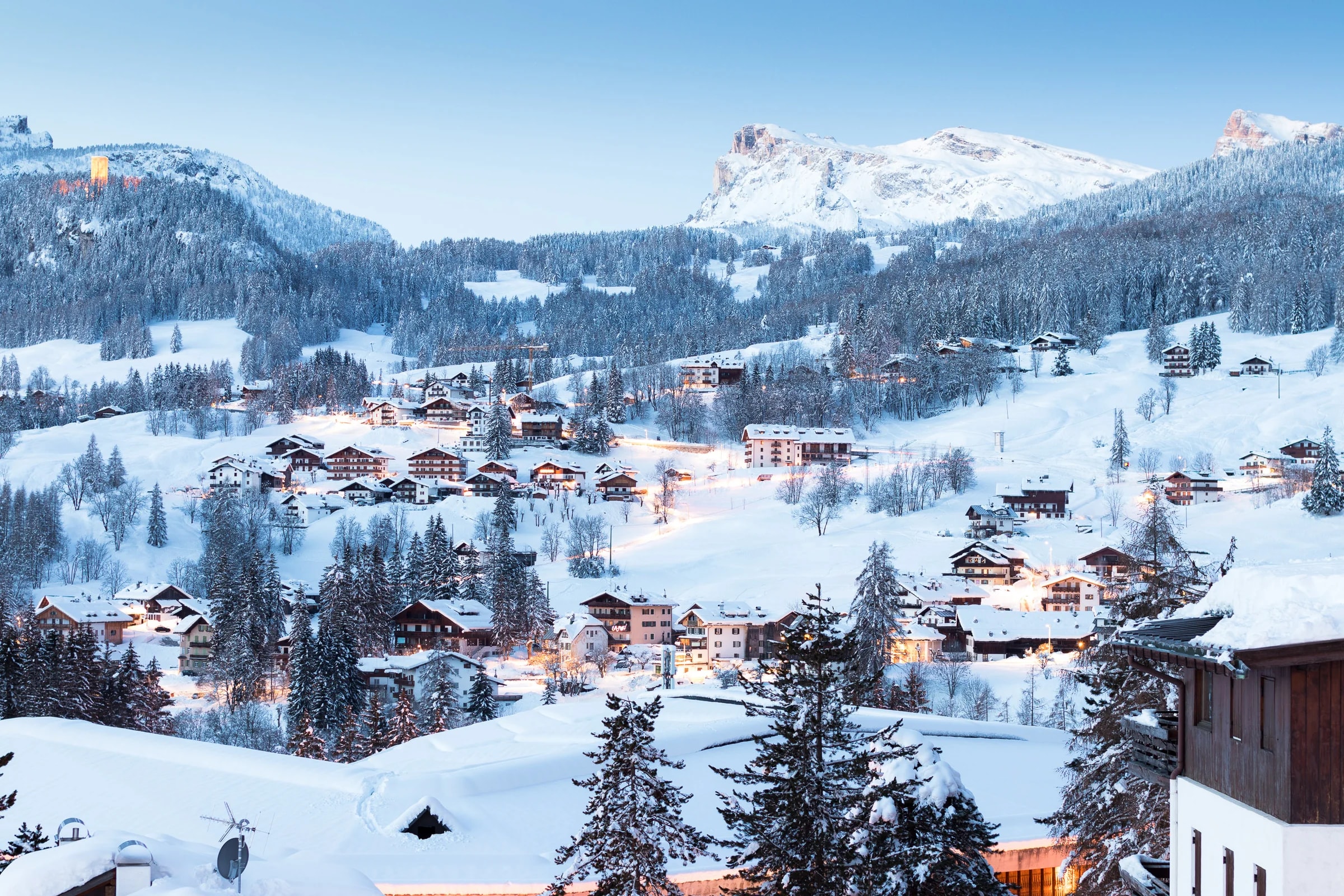 Verschneite Chalets im Weiler Ronco in Cortina d'Ampezzo bei Tagesanbruch, dahinter Gipfel der Dolomiten.