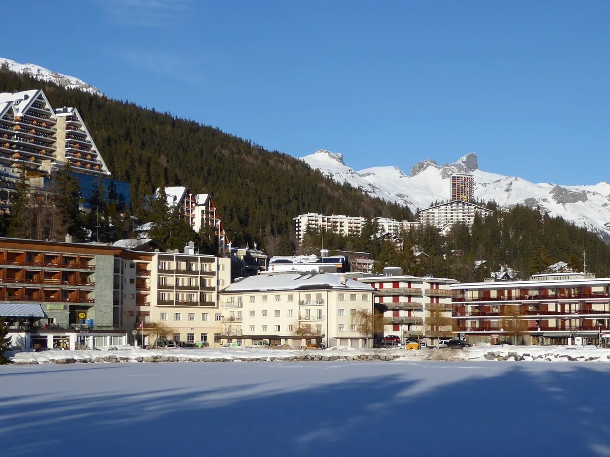 Hotels von Crans-Montana an einem zugefrorenen, verschneiten Teich unter blauem Januarhimmel.