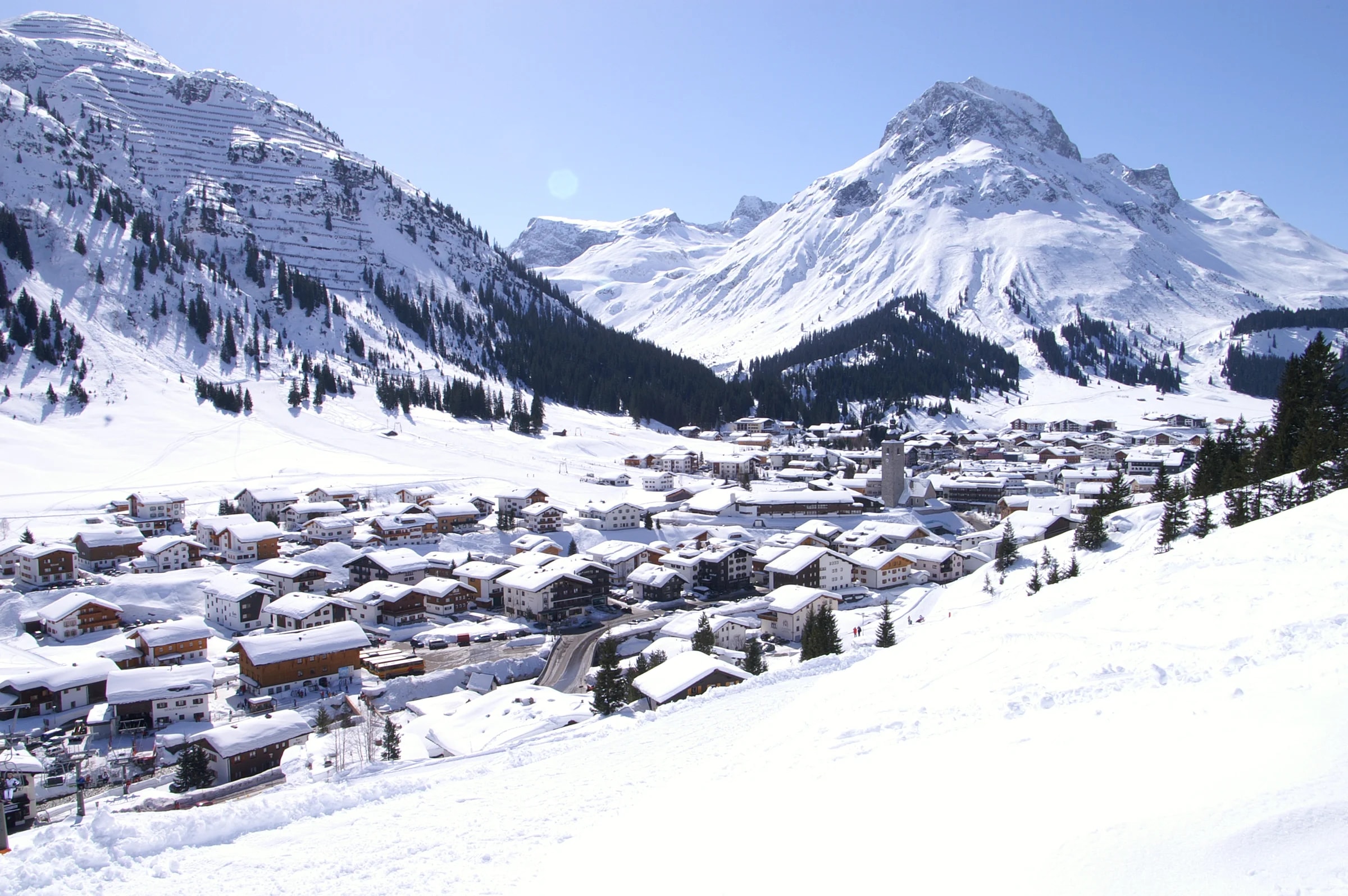 Lech am Arlberg under deep snow, with the Omeshorn behind and a blue sky.