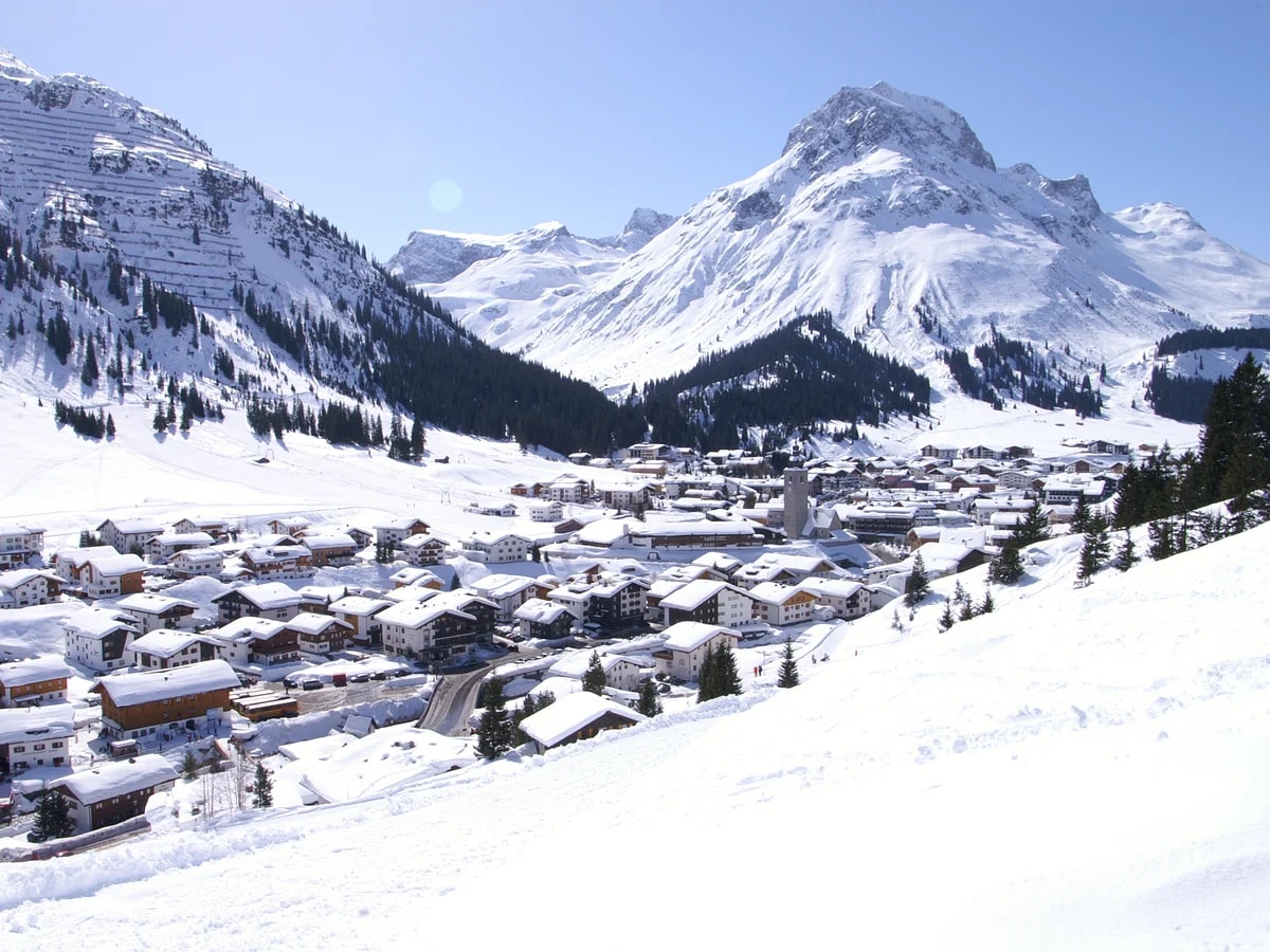 Lech am Arlberg unter einer dicken Schneedecke, dahinter das Omeshorn und blauer Himmel.
