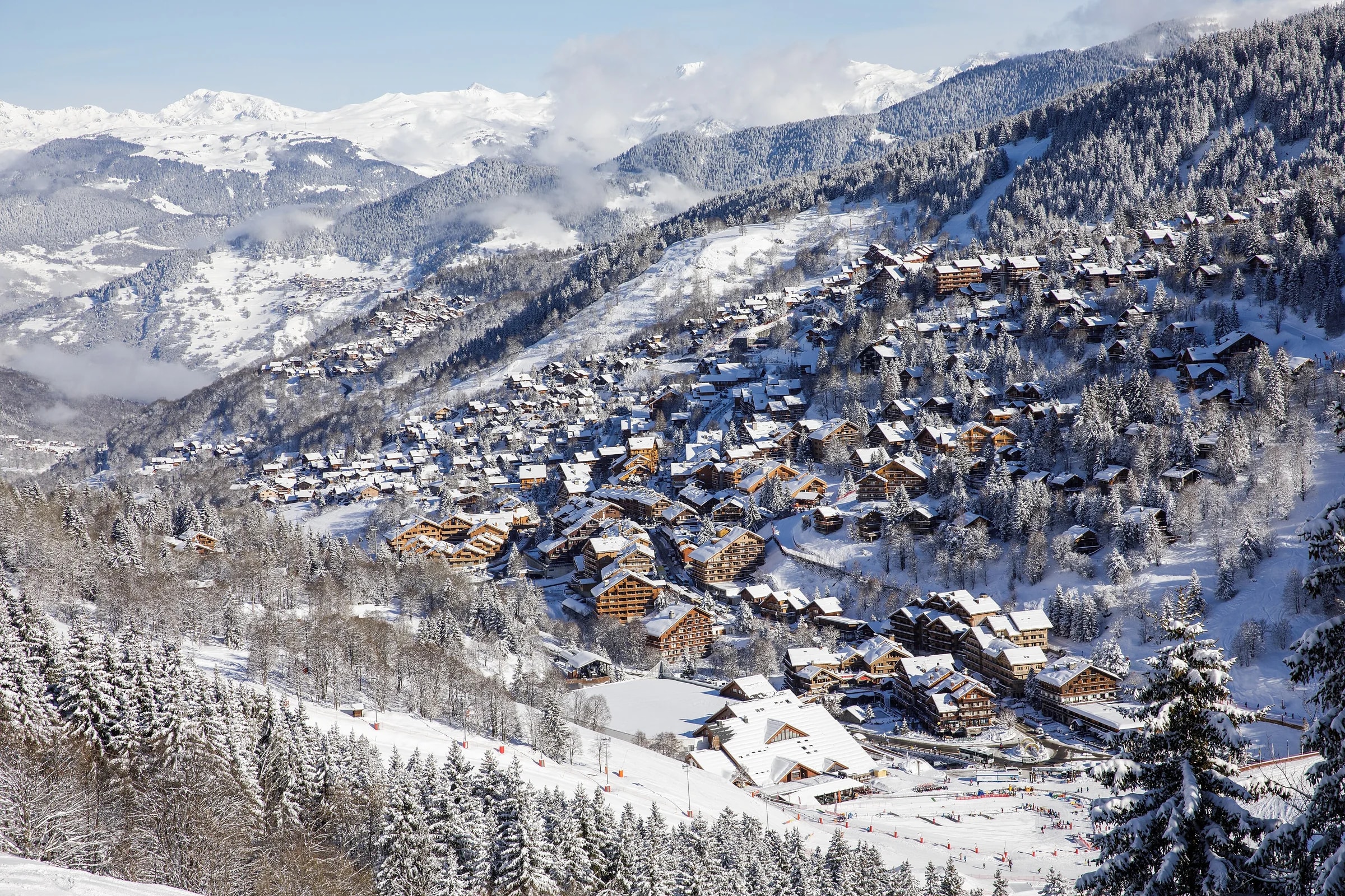 Das verschneite Dorf Méribel von oben, mit Holzchalets zwischen den Tannen.