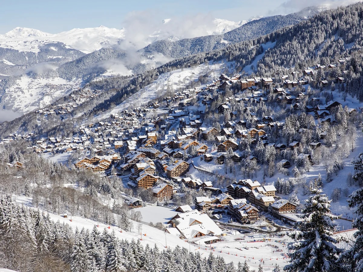 Das verschneite Dorf Méribel von oben, mit Holzchalets zwischen den Tannen.