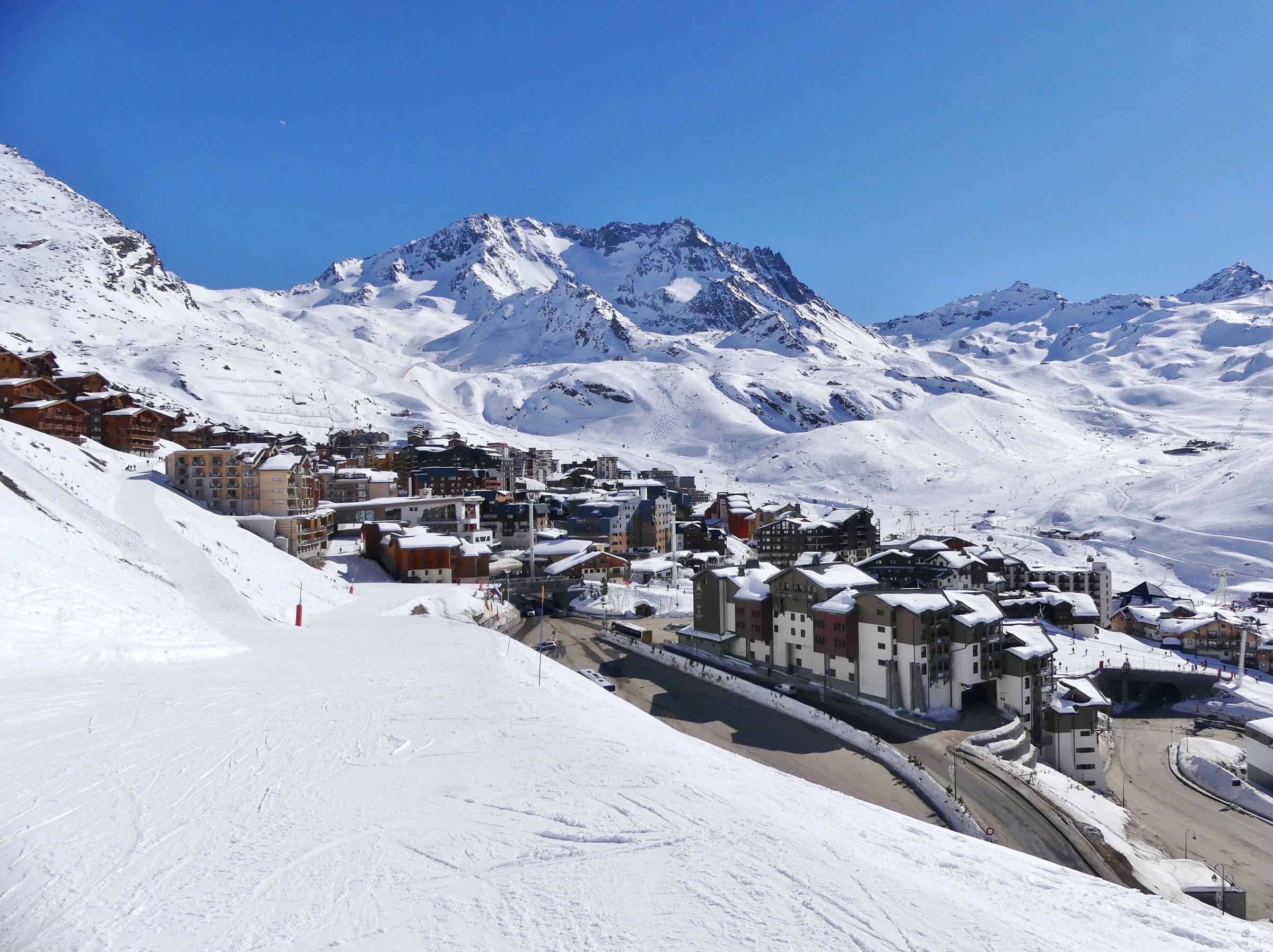 Der verschneite Skiort Val Thorens von Nordwesten, mit Gipfeln unter blauem Himmel.