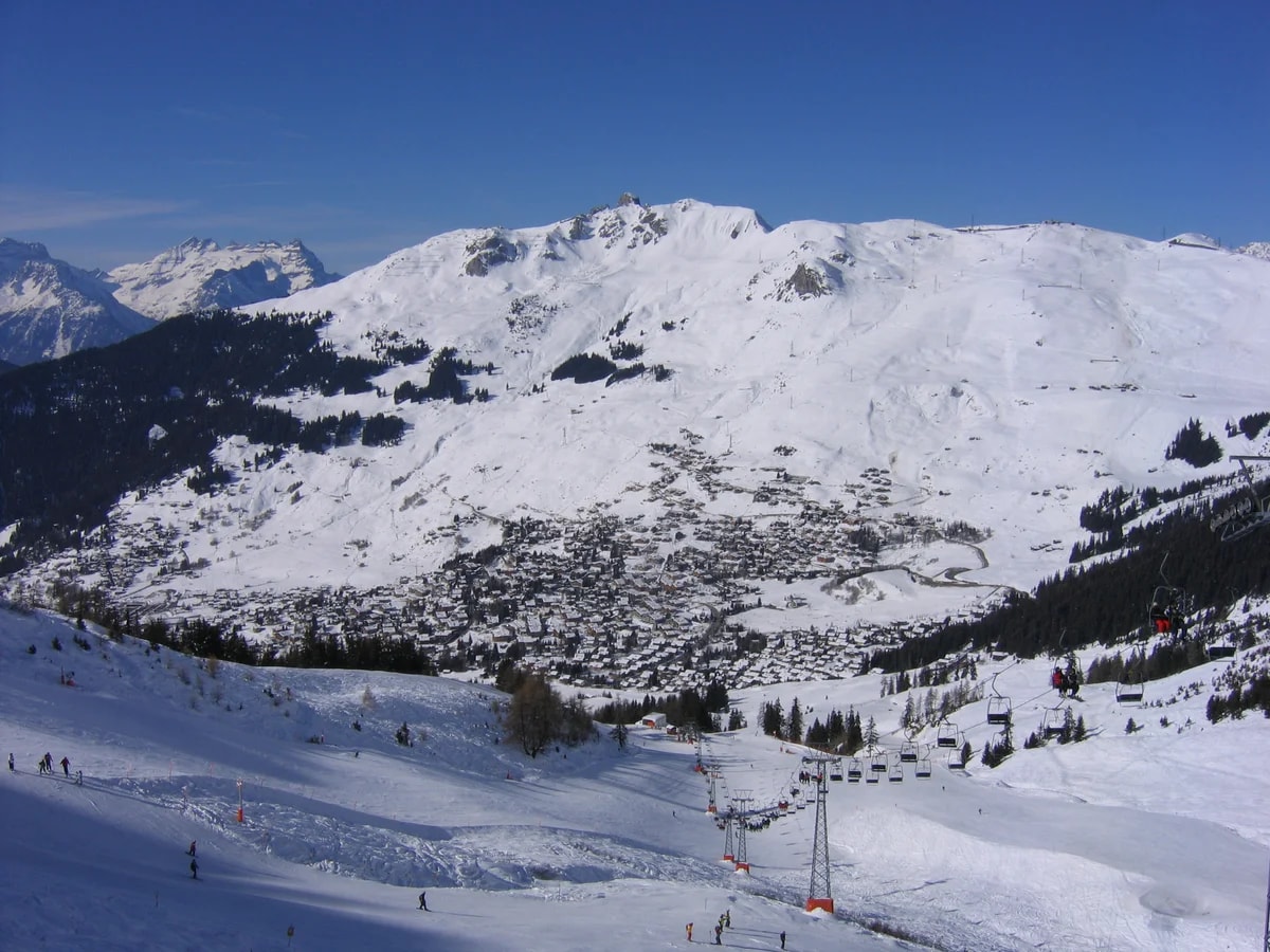 Verbier und sein Skigebiet im Schnee, von der Piste aus gesehen, mit einem Sessellift im Vordergrund und blauem Himmel.